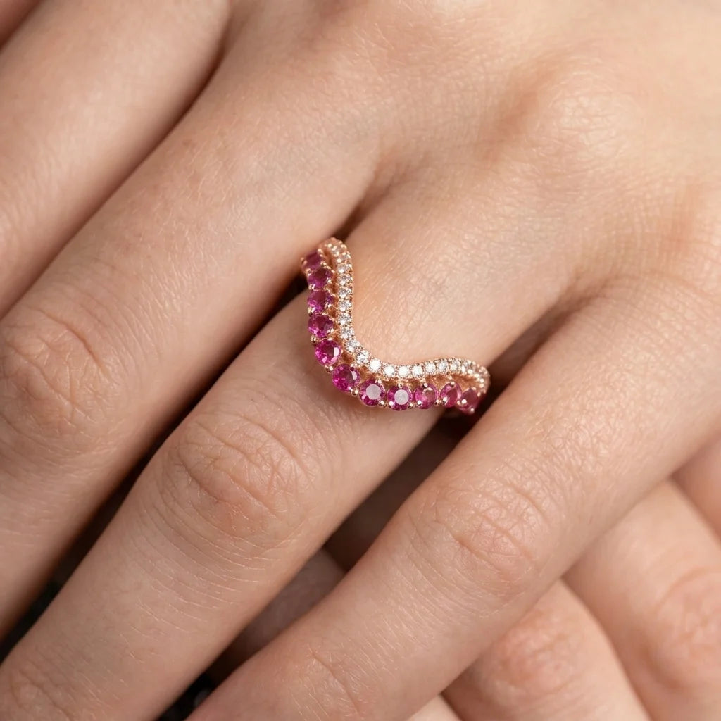 A close-up of a hand wearing a curved rose gold ring adorned with alternating rows of pink gemstones and clear stones.