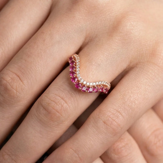 A close-up of a hand wearing a curved rose gold ring adorned with alternating rows of pink gemstones and clear stones.