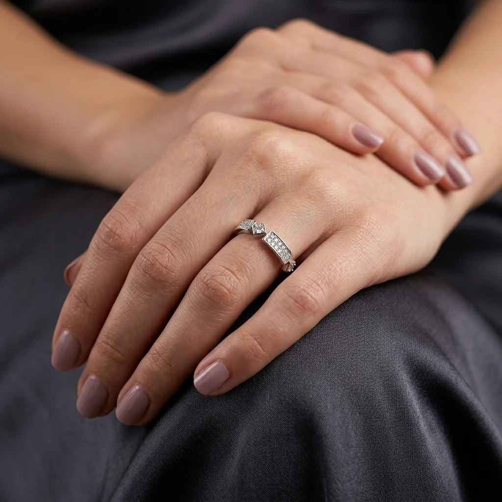 A close-up of a woman's hands resting on dark gray fabric, wearing a silver ring with a small clear gemstone on one finger.