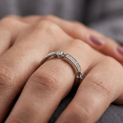 A close-up of a silver ring with a split design, featuring a central square-cut gemstone and a curved pavé band, worn on a person's finger.