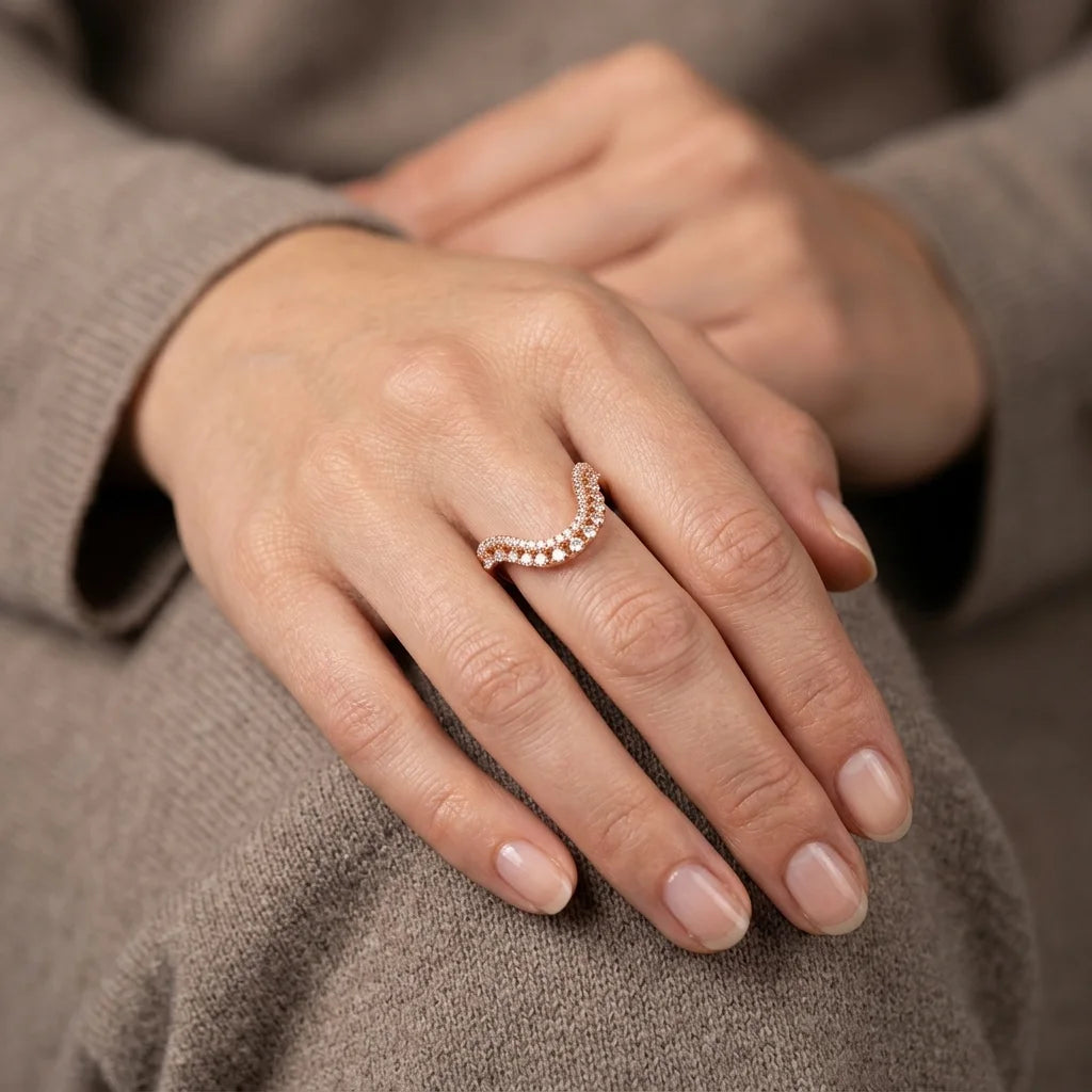 A close-up of a person's hand wearing a delicate rose gold ring with small clear stones, set against a soft gray knit sweater.