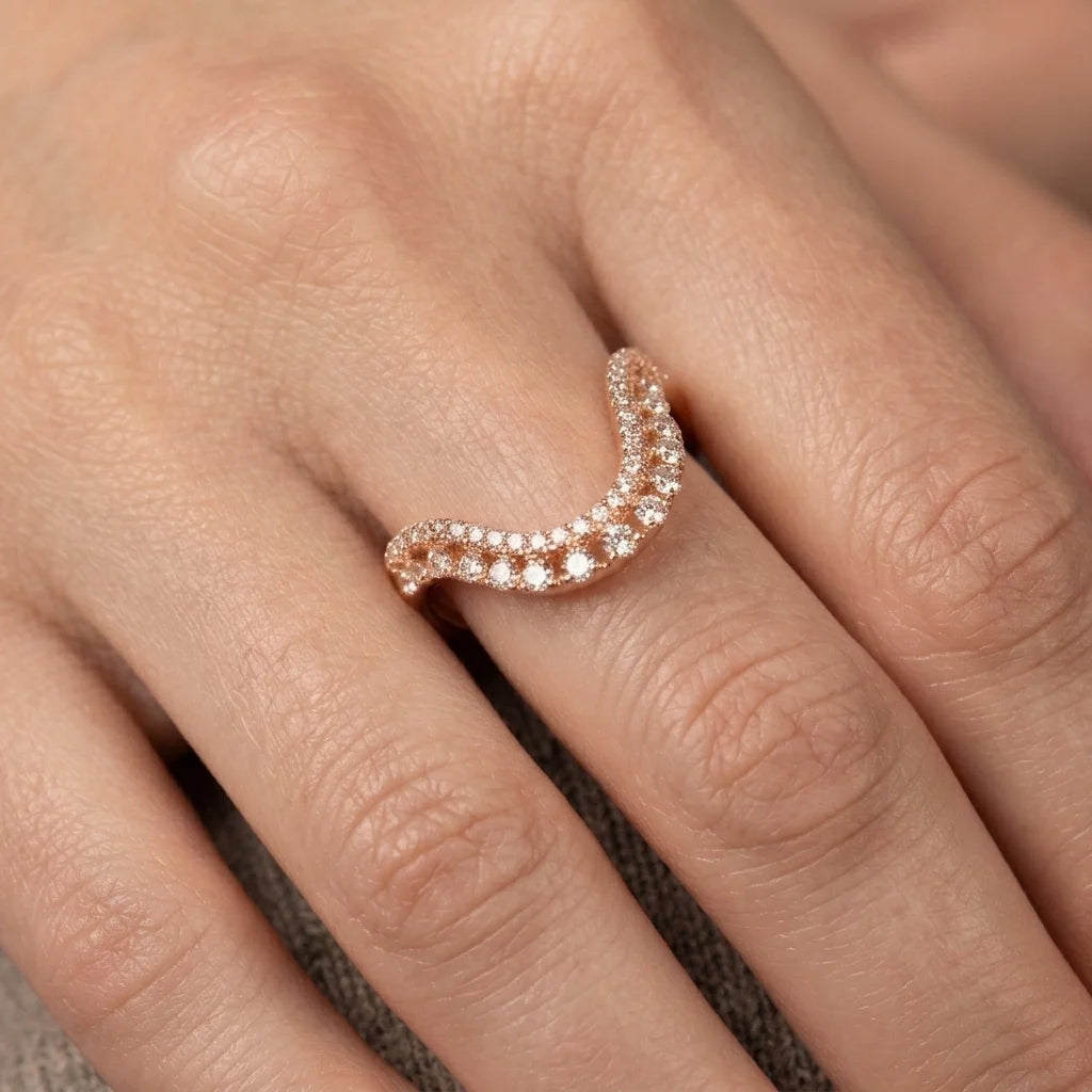 A close-up of a hand wearing a curved rose gold ring set with small clear stones.