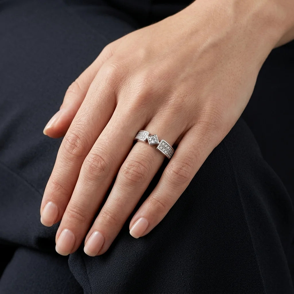 A close-up of a hand wearing a silver ring with three marquise-cut diamonds and pavé-set diamonds on a dark navy background.