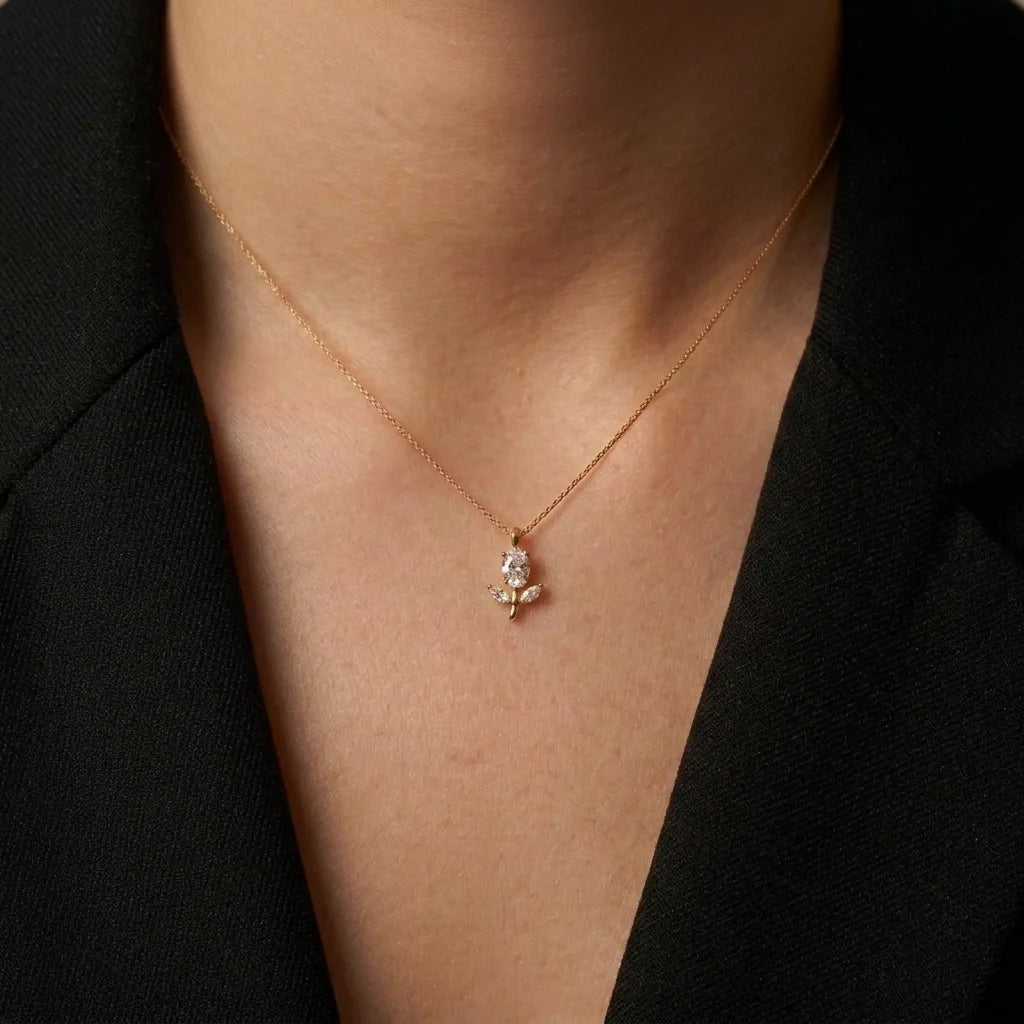 A delicate rose gold chain necklace with a small floral pendant, worn by a model in a black blazer.