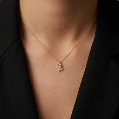 A delicate rose gold chain necklace with a small floral pendant, worn by a model in a black blazer.