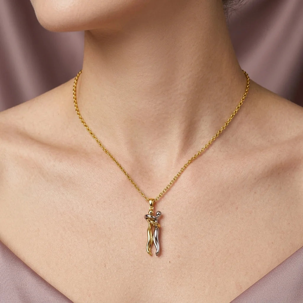 A close-up of a model's neck and chest wearing a delicate gold chain necklace with a small pendant shaped like a stylized female figure in gold and silver.