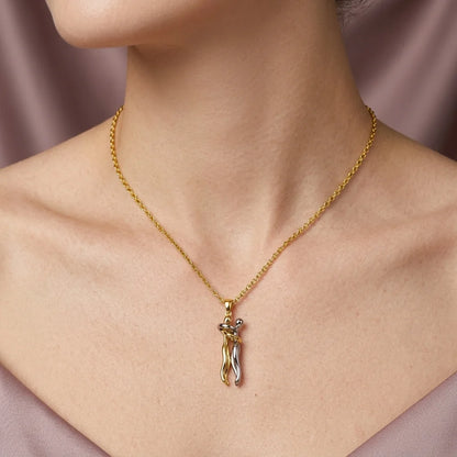 A close-up of a model's neck and chest wearing a delicate gold chain necklace with a small pendant shaped like a stylized female figure in gold and silver.