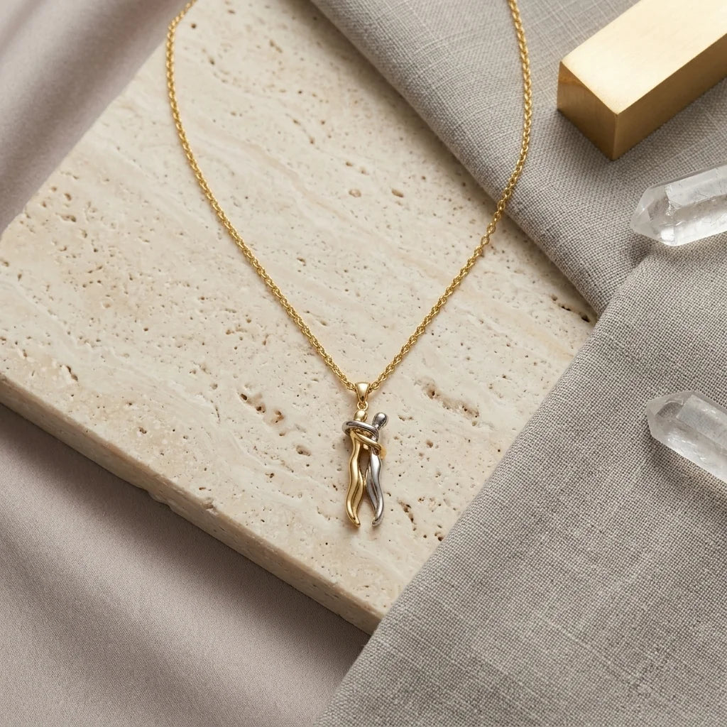 A delicate gold chain necklace with a small twisted pendant, styled on a beige stone slab and gray linen fabric with clear crystal points and a gold block.