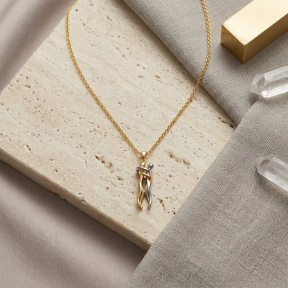 A delicate gold chain necklace with a small twisted pendant, styled on a beige stone slab and gray linen fabric with clear crystal points and a gold block.