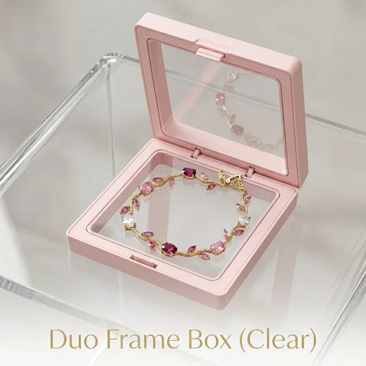 A pink open frame jewelry box with a clear lid, displayed on a clear acrylic stand. Inside the box is a gold bracelet decorated with pink and clear rhinestones.