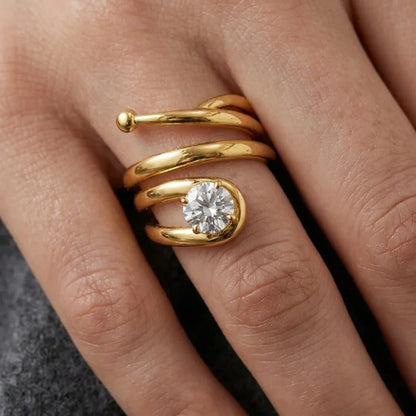 Close‑up of a gold spiral ring with a round diamond gemstone on a hand.