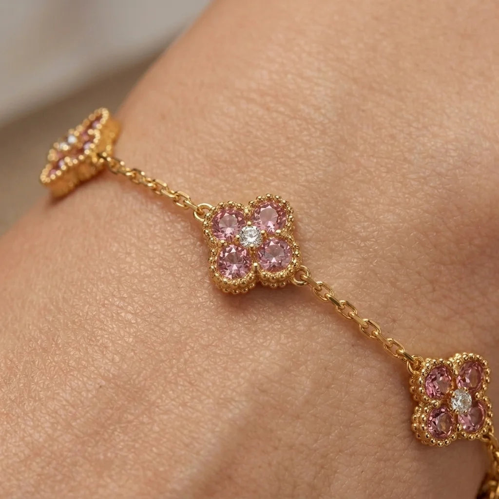 A gold chain bracelet with three floral clover motifs, each set with pink gemstones and a clear center stone, shown worn on a wrist.