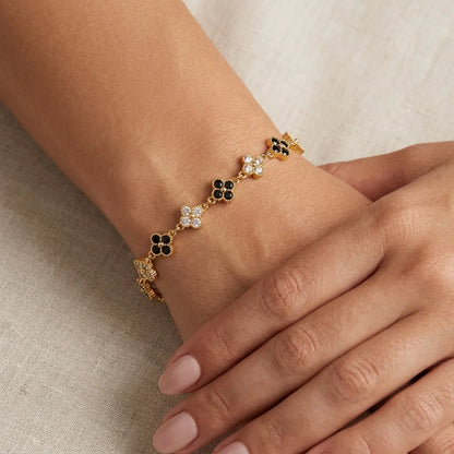 Gold-plated clover bracelet with black and white cubic zirconia four-leaf stations and adjustable chain on ivory satin