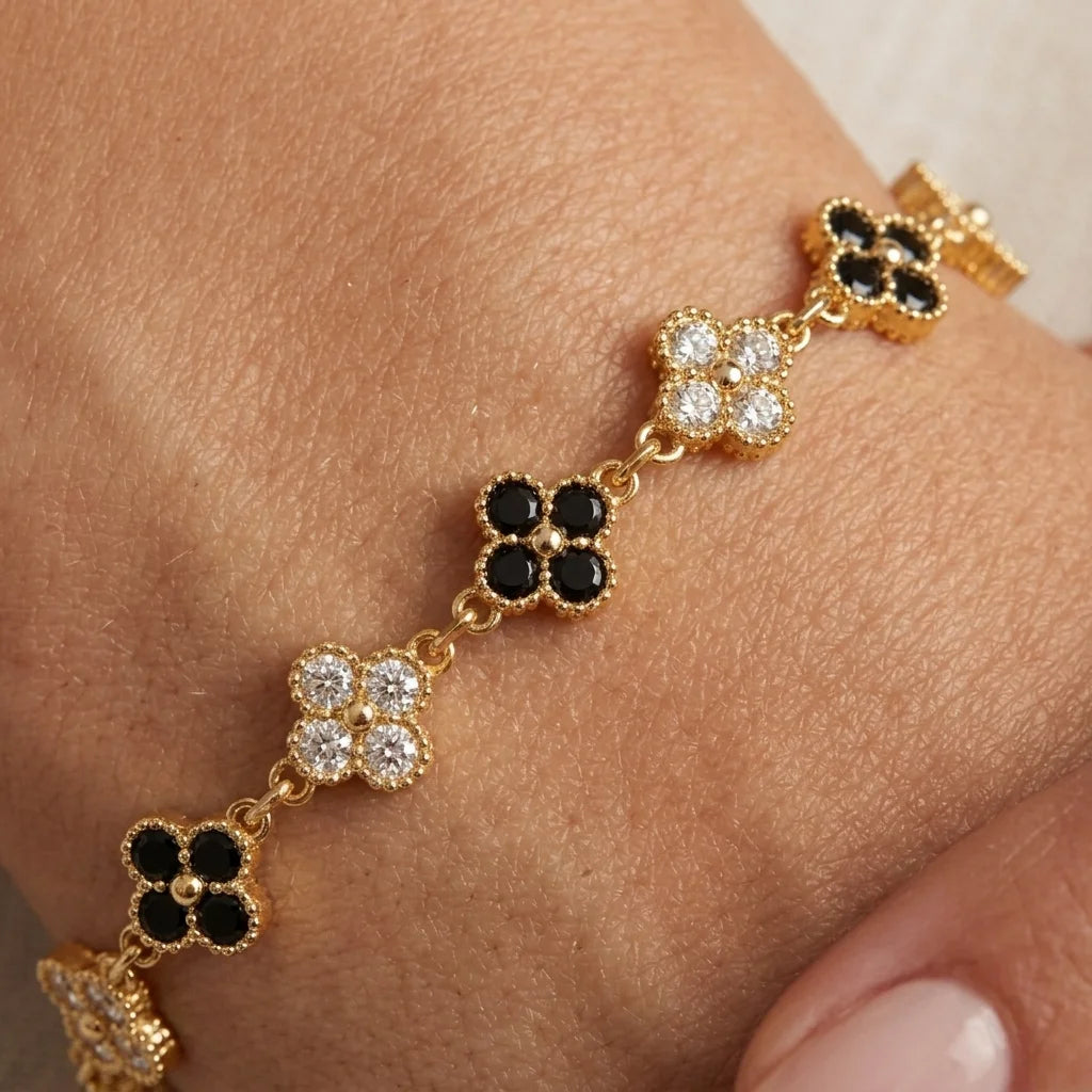 Black and white clover bracelet in gold plating with lobster clasp and extender chain, flat lay on cream silk