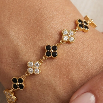 Black and white clover bracelet in gold plating with lobster clasp and extender chain, flat lay on cream silk