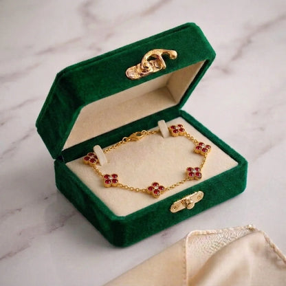 A gold chain bracelet with colorful gemstone accents displayed inside an open dark green velvet jewelry box on a light marble surface.