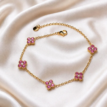 A gold chain bracelet with five floral motifs, each set with pink gemstones and small clear stones, displayed on a draped cream satin fabric.