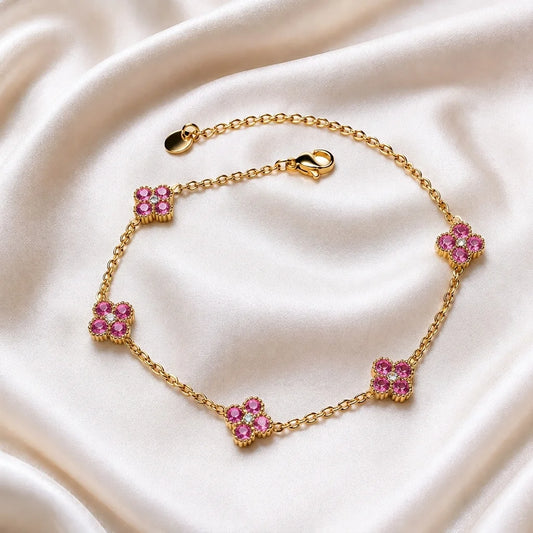 A gold chain bracelet with five floral motifs, each set with pink gemstones and small clear stones, displayed on a draped cream satin fabric.