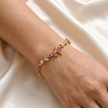 Rose-pink zircon blooms on a warm gold-tone vine with a tiny bow. The bracelet made for gifting.